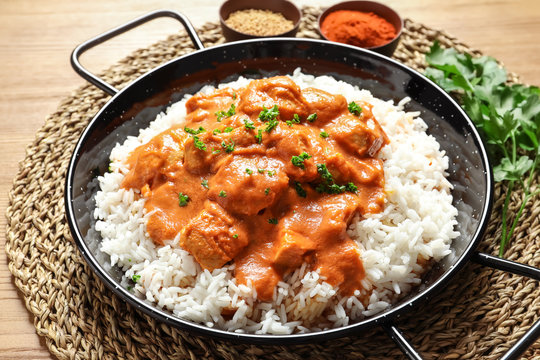 Delicious butter chicken with rice in dish on wooden table