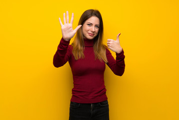 Woman with turtleneck over yellow wall counting six with fingers