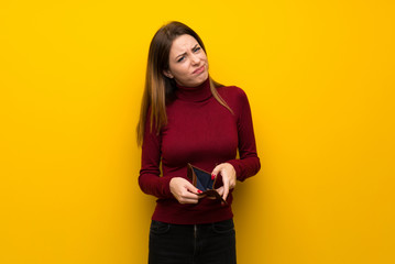 Woman with turtleneck over yellow wall holding a wallet - obrazy, fototapety, plakaty