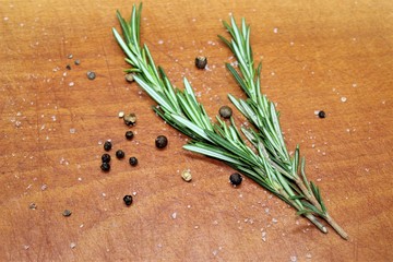 Sprigs of rosemary, laid on a cutting wooden board with black and allspice peas.