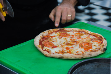 Ready-made Italian pizza on a thin dough, cooked on special equipment, the chef cuts the pizza into...