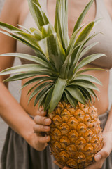 woman in boho clothes keep the tropical fruit pineapple in hands on the light background in Bali
