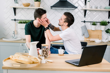 Happy gay couple drinking coffee and having fun together. Everyday morning routine of gay couple life in kitchen at home. Gay concept, happy life