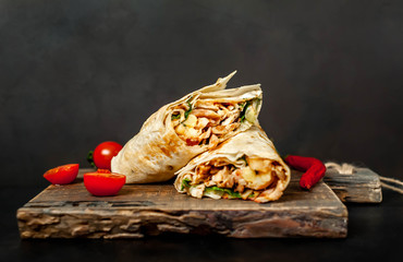 Burrito wraps with chicken and vegetables on a cutting board, against a background of concrete,...