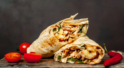 Burrito wraps with chicken and vegetables on a cutting board, against a background of concrete,...