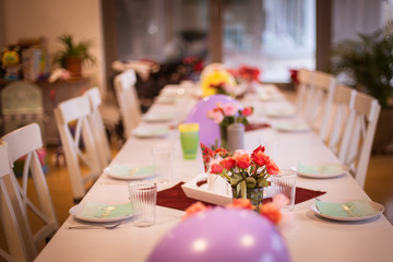 Tisch gedeckt für eine Geburtstagsfeier, dekoriert mit bunten Luftballons und Blumen