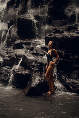 beautiful woman with brunette hair in black swimwear posing  on background of waterfall in Bali