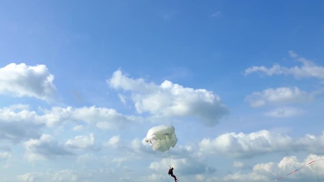 Unrecognizable skydiver with parachute flies against the blue sky with white clouds on summer day.