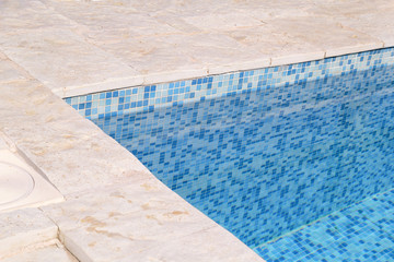Blue ripped water in swimming pool in tropical resort with edge of pavement. Part of Swimming pool bottom background. Clear light blue pool water ripples with sun reflection. Surface of swimming pool.