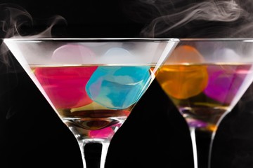 wine glasses with colored ice cubes and floated ice vapor on black background. Selective focus