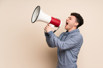 Young man over isolated wall shouting through a megaphone