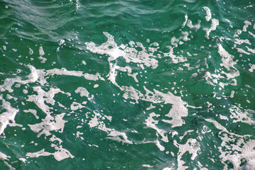 Turquoise green seawater with sea foam as background, close up. Surface of sea with waves, splash, foam and bubbles, blue abstract texture and wallpaper. Beautiful green waves with a lot of sea foam.