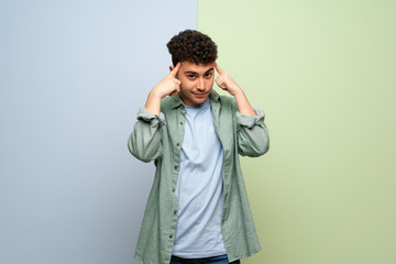 Young man over blue and green background having doubts and thinking