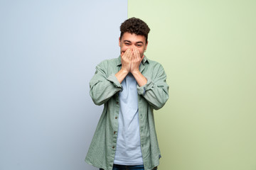 Young man over blue and green background smiling a lot while covering mouth