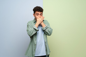 Young man over blue and green background covering mouth with hands for saying something inappropriate