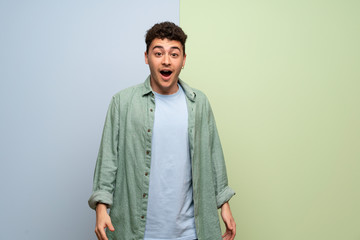 Young man over blue and green background with surprise and shocked facial expression