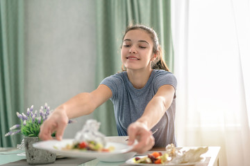 young teen girl sits at the dinner table and serves a plate of food for family members