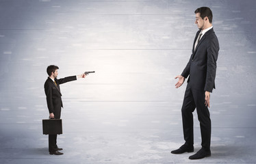 Fototapeta premium Tiny businessman with gun shooting giant fearful businessman 