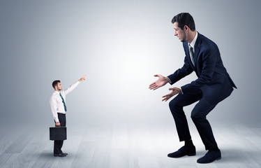 Small businessman in shirt pointing to an afraid businessman
