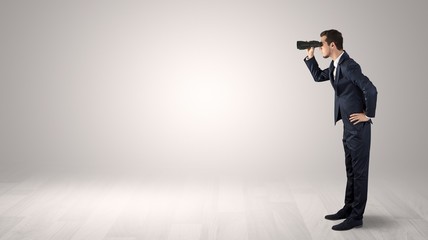 Businessman looking forward with binoculars in an empty space
