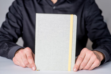 person.shows a closed notebook. Place for the text on the cover of a closed notebook. Mockup of Notebook