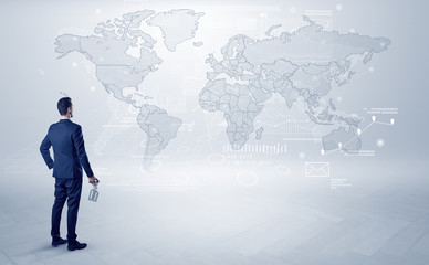 Businessman standing with his back and looking at a worldwide map with objects in his hand
