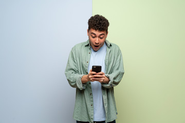 Young man over blue and green background surprised with a mobile