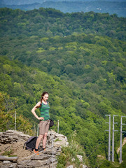 A girl stands on a cliff against the background of green forest