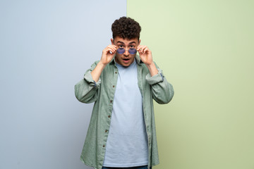 Young man over blue and green background with glasses and surprised