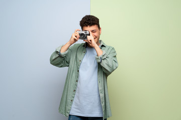 Young man over blue and green background holding a camera