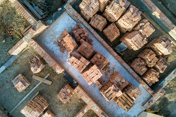 Concrete foundation of basement or first floor of future house with stacks of red bricks for walls construction on sunny summer day, aerial view.