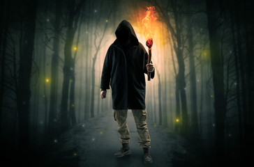 Mysterious man coming from a path in the forest with burning flambeau concept
