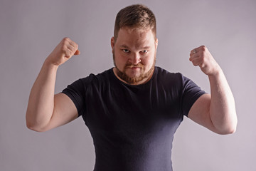 Portrait of attractive young sporty man in black t-shirt standing with arm up, showing muscles isolated on gray background. Hard light