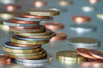 Pile of shiny coins different sizes and colors stacked unevenly on each other on colorful blurred blue abstract background. Money saving and financial risk concept.