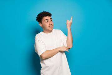 Young man over blue background pointing a great idea and looking up