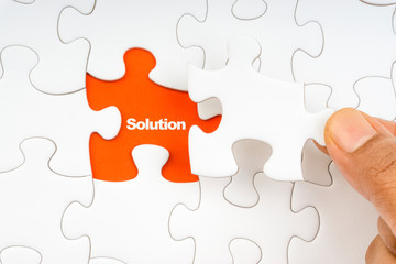 Fototapeta premium Hand holding piece of jigsaw puzzle with word SOLUTION. Selective focus