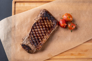grilled steak with tomatoes on a wooden board, close-up, top view