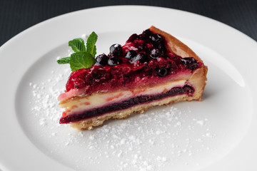 slice of cheesecake with berry jelly and mint on a white plate, close-up