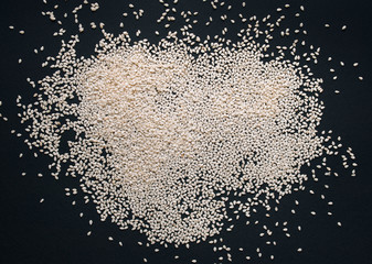 White sesame seeds on black textured paper background. Close up, copy space.