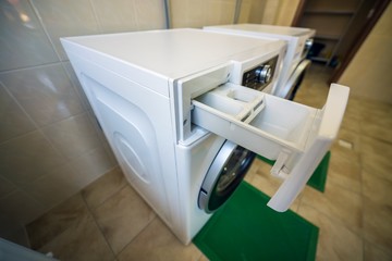 Modern new industrial washing machines in clean tiled bathroom or laundry room on rubber insulation mats.