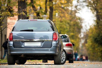 Gray shiny car parked in quiet area on asphalt road on blurred bokeh background on bright sunny day. Transportation and parking concept.