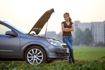 Young woman and a car with popped hood. Transportation, vehicles problems and breakdowns concept.