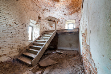 Large spacious forsaken empty basement room of ancient building or palace with cracked plastered brick walls, small windows, dirty floor and wooden staircase ladder.