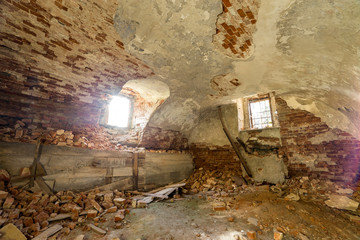Old forsaken empty basement room of ancient building or palace with cracked plastered brick walls, low arched ceiling, small windows with iron bars and dirty floor.