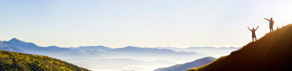 Small dark silhouettes of tourist travelers on steep mountain slope at sunrise on copy space...