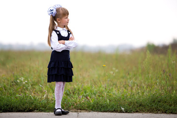 Full-length portrait of cute adorable serious thoughtful first grader girl in school uniform and...