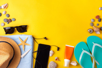 Sun glasses, sun screen, headphones, smartphone, towel, slippers. Flatlay beach vacation on a yellow background.