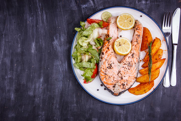 Fried salmon with lemon, potatoes, salad and spices on a black wooden table
