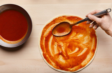 Man spreading tomato paste on pizza base