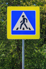 Road sign of Crosswalk on a gray pillar against green tree in sunny summer day
